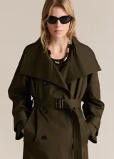 Abrigo tipo trench de diseño oversize y corte recto, color verde militar. Presenta cuello de solapa ancha, cierre frontal de doble botonadura, cinturón desmontable con hebilla y bolsillos laterales. Incluye trabillas en los puños y forro interior.
