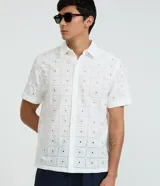 Camisa de manga corta para hombre, confeccionada en algodón color blanco con diseño de bordado de flores y perforaciones geométricas. Presenta cuello inglés y cierre frontal con botones.