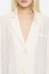 Chaqueta estilo sastre color blanco, confeccionada en mezcla de lino. Presenta escote con solapas, manga larga recta con abertura en puño, cierre con botonadura frontal y bolsillos con vivo.