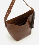 Bolso tipo bucket grande Satinato en color marrón, confeccionado en PU. Presenta asa de hombro ajustable, herrajes metálicos dorados, detalle de borla decorativa lateral con textura símil serpiente y un pequeño monedero o estuche removible con cierre unido por una tira.