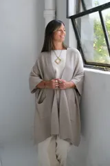 Poncho abierto de tejido de punto en color visón, con diseño holgado, mangas cortas y bolsillos frontales aplicados.