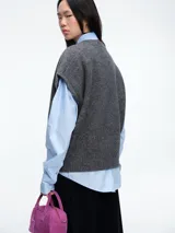 Chaleco de tejido de punto color gris, con cuello redondo y cierre frontal completo a contratono en color celeste. Presenta un diseño sin mangas con terminaciones acanaladas en cuello, sisas y ruedo.
