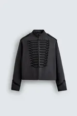 Chaqueta cropped de algodón con cuello mao y manga larga. Presenta un diseño de inspiración militar con alamares decorativos en contraste en el frente, trabillas en los hombros y cierre frontal con ganchos metálicos.