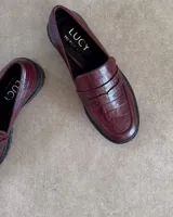 Mocasines negros de estilo clásico con textura de cuero grabado tipo cocodrilo. Presentan una banda frontal característica y suela plana con borde definido.