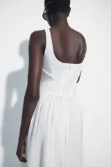 Vestido midi de corte corsetero color blanco, con escote redondo, tirantes finos y detalle de lazo en el delantero. Falda con frunces y cierre en la espalda con cremallera oculta.