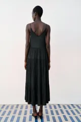Vestido midi negro satinado con escote en pico, tirantes finos y detalle de lazada frontal. Presenta diseño de paneles fruncidos.