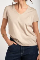 Remera color beige de algodón peinado, con escote en V y detalle de ribete dorado brillante en el cuello, mangas cortas y corte al cuerpo.