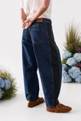 Pantalón jean de corte barrel en azul oscuro con paneles laterales negros, diseño de tiro alto y costuras decorativas en las rodillas.