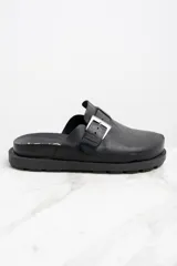 Zueco negro de cuero con hebilla metálica plateada ajustable y suela track.