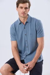 Camisa de piqué lisa color celeste, de manga corta, con cuello camisero y cierre frontal de botones oscuros.