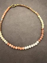 Collar de cuentas esféricas de piedras naturales en tonos rosados, beige y blanco, con cierre de mosquetón metálico dorado.