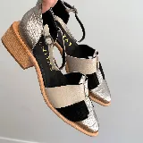 Zapato cerrado tipo sandalia de Vanitas, confeccionado en cuero vacuno. Presenta un diseño tricolor con paneles en negro, beige y detalles en cuero plateado con textura de reptil. Cuenta con punta fina, taco de madera de 4 cm y cierre con pulsera al tobillo.