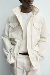 Cazadora técnica de corte relaxed fit, color beige, con cuello subido, manga larga y acolchado interior. Cuenta con múltiples bolsillos frontales con solapa, cintura ajustable con cordón interior y cierre frontal de cremallera oculta por solapa con botones a presión.