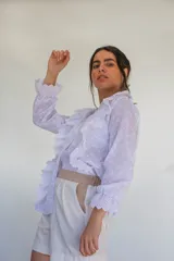 Camisa blanca de algodón estilo romántico con tejido broderie, mangas largas con puños volados y detalles de volados frontales.