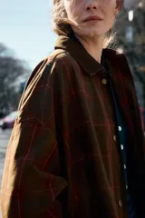 Chaqueta de mujer de la colección Zara Woman, confeccionada en algodón 100% con acabado encerado. Presenta un estampado a cuadros en tonos marrón y rojo, cuello solapa de pana, manga larga con puño y botón, bolsillos de plastrón con solapa en el delantero y cierre frontal con botones a presión.