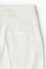 Pantalón de tiro alto con piernas amplias y corte recto. Presenta cierre frontal con botón oculto, bolsillos laterales al bies y bolsillos traseros insertados, con pliegues marcados en la parte delantera y trasera.