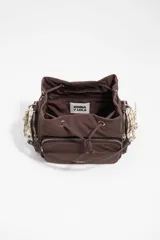 Bolso bandolera de nailon marrón de Bimba y Lola, con cierre de cordón ajustable, bolsillo frontal con cremallera y el logotipo de la marca impreso. Cuenta con una correa ajustable ancha de lona beige y detalles de cuerdas decorativas en los laterales.
