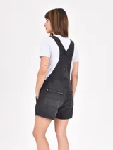 Monoprenda short de jean negro con efecto gastado, tirantes ajustables con hebillas metálicas y bolsillos frontales.