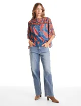 Blusa de gasa con estampado de arabescos en tonos azules y rojos, con cuello a la base y mangas tipo capa. Presenta una silueta holgada con ruedo elástico en punto smock que ajusta a la cintura.