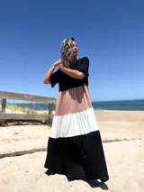 Vestido largo de diseño tricolor con bloques de color en negro, beige y crudo. Presenta escote en V, mangas cortas con volados y una falda amplia con cortes horizontales que crean un efecto escalonado.