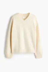 Buzo oversized de punto suave, color beige, con escote en V acanalado, hombros caídos y mangas largas. Cuenta con ribetes acanalados en los puños y en el dobladillo inferior.