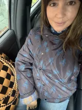 Campera acolchada impermeable color marrón oscuro con estampado a cuadros y flores azules, cuello camisero, bolsillos laterales y cierre frontal con broches a presión.