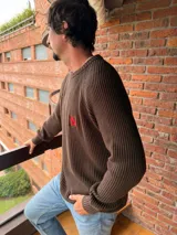 Sweater de tejido de punto acanalado en color marrón, con cuello redondo, mangas largas y bordado distintivo en color rojo en el pecho.