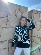 Sweater negro con estampado abstracto en blanco y detalles en verde.