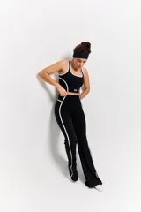 Conjunto deportivo compuesto por un top de escote redondo y calzas de tiro alto con diseño acampanado. Ambas piezas son de color negro con detalles de costuras blancas en contraste y logo estampado en el frente del top.
