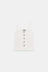 Top blanco de punto acanalado, con escote cuadrado y tirantes anchos. Presenta un cierre frontal decorativo con cinco botones metálicos plateados con forma irregular. El bajo es asimétrico y redondeado.