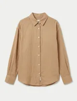 Camisa de manga larga con cuello clásico y cierre frontal de botones. Presenta un diseño de corte holgado con hombros caídos y puños abotonados.