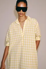 Vestido midi camisero de algodón, color amarillo con estampado a cuadros. Cuenta con cuello solapa, escote en V, mangas cortas con puño y bolsillos laterales ocultos en la costura, con diseño evasé.