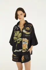 Camisa de manga corta negra con cuello camisero, cierre frontal de botones y diseño holgado, decorada con estampados botánicos y gráficos de estilo vintage.