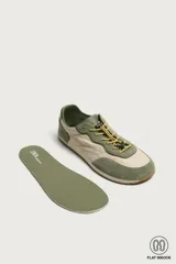 Zapatilla deportiva barefoot fabricada en combinación de piel y tejido, en tonos verde oliva y beige, con cordones elásticos amarillos y suela de goma flexible.