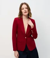 Blazer de sastrería en crepé color bordó, con cuello solapa, cierre frontal de un solo botón metálico y bolsillos con solapa. Presenta mangas largas con detalle de tres botones decorativos en los puños.