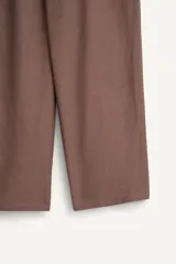 Pantalón de corte relajado confeccionado en tejido fluido con mezcla de viscosa y lino. Presenta un diseño cruzado en la cintura con cierre de cremallera, botón y trabilla ajustable. Cuenta con bolsillos laterales y bolsillos traseros de vivo con botón.