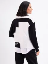 Buzo de tejido de punto con diseño geométrico en bloques de color blanco y negro, cuello redondo y mangas largas.