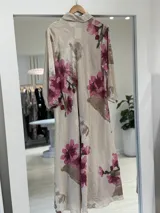 Vestido largo beige de corte camisero con estampado floral en tonos fucsia y marrón, cuello camisero, cierre frontal con botones y mangas largas.