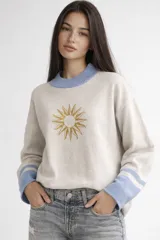 Sweater de algodón de corte holgado con cuello redondo. Presenta un diseño jacquard con un sol bordado en el centro, cuello en color celeste y puños con franjas celestes.