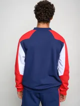 Buzo de felpa con diseño de bloques de color, predominantemente rojo en el cuerpo y azul marino en las mangas y hombros. Presenta el escudo del Club Nacional de Football y el logo de Umbro en el pecho.