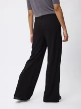 Pantalón de corte recto y pierna ancha, color beige, con cintura de tiro medio y cierre frontal.
