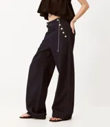 Pantalón wide leg de jean azul oscuro, de talle alto con calce amplio y detalles de botones dorados en el lateral frontal.