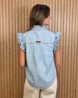 Musculosa de jean celeste sin mangas, con cuello alto fruncido, cierre frontal con botones y detalles de volados en las sisas y a lo largo de la botonera.