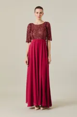 Vestido largo de fiesta color bordó, con cuerpo superior bordado en lentejuelas al tono, mangas cortas tipo capa y falda fluida de corte evasé con cintura definida.