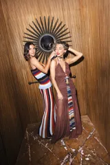 Vestido largo de punto con diseño a rayas horizontales en tonos azul, marrón y mostaza, con toques de brillo. Presenta corte ajustado en la parte superior con tirantes y falda larga con vuelo y movimiento.