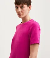 Blusa blanca de poliéster con cuello redondo, mangas cortas, cierre trasero en forma de gota, pequeñas aberturas laterales y acabados en pespuntes en las mangas y el cuello.