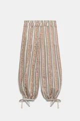 Pantalón bombacho de tiro medio con estampado de rayas verticales en tonos tierra y beige. Presenta aplicación de lentejuelas, cinturón del mismo tejido, forro interior tipo shorts y bajo acabado en puño con lazada. Cierre lateral con cremallera oculta.