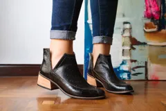 Botín de cuero blanco con textura de crocco y charol, diseño con calados circulares y aberturas laterales en forma de V. Cuenta con taco foliado de madera y vira cosida.
