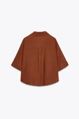 Camisa de lino color celeste claro, con cuello solapa, escote pico, manga corta con vuelta y dos bolsillos de plastrón en el delantero. Cierre frontal con botones.