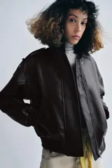 Chaqueta bomber de efecto piel en color marrón oscuro, con cuello solapa, cierre frontal con cremallera y botones, bolsillos delanteros, trabillas en los hombros y puños y bajo elásticos.